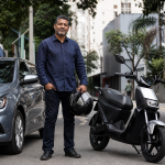 Motorista profissional ao lado de carro novo e motocicleta elétrica em rua urbana