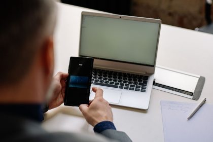 Profissional usa o celular para realizar um pagamento digital ao lado de um laptop em um escritório.