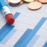 Gráficos de barras ao lado de moedas e um lápis, simbolizando análise financeira.