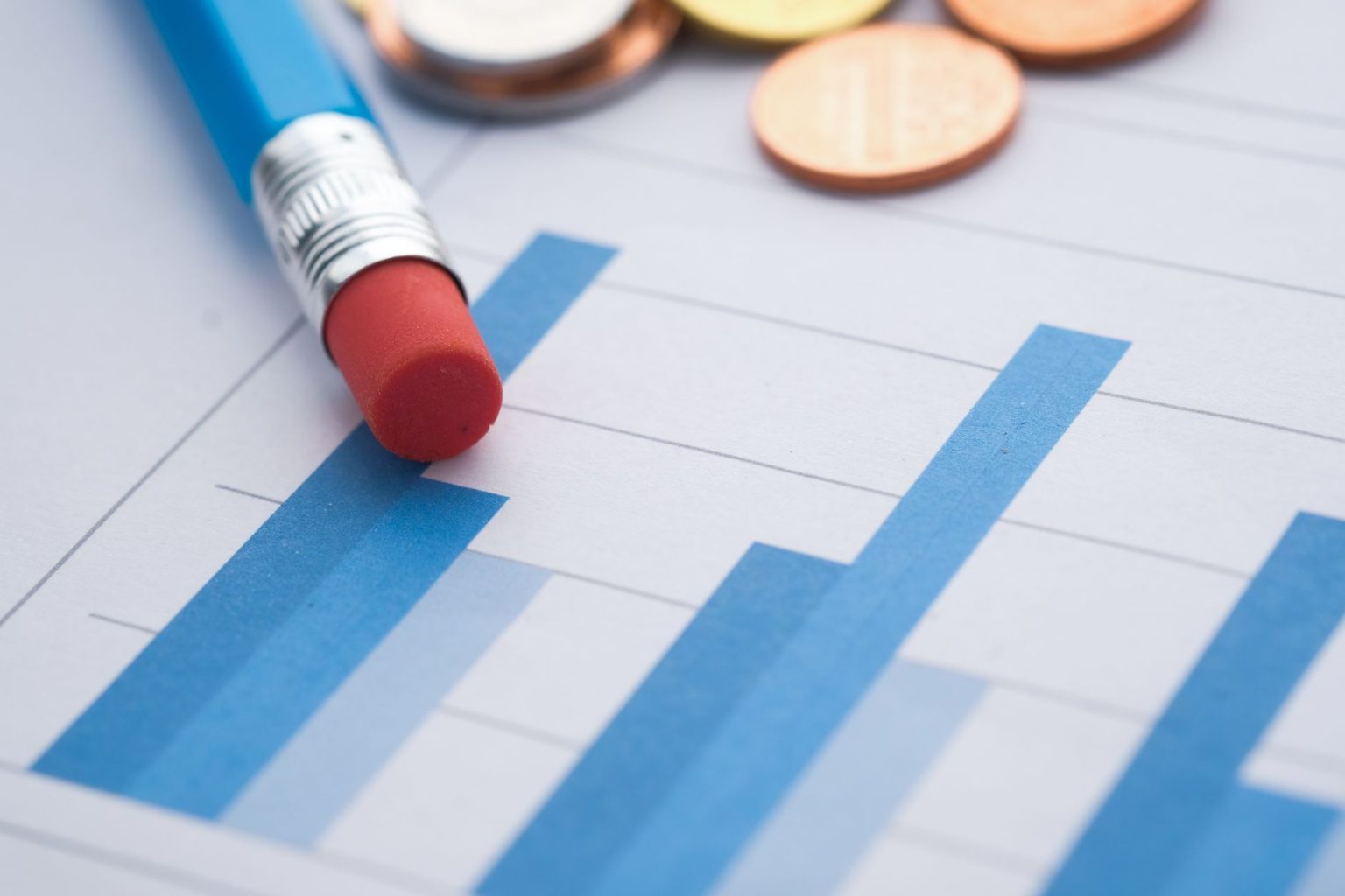 Gráficos de barras ao lado de moedas e um lápis, simbolizando análise financeira.